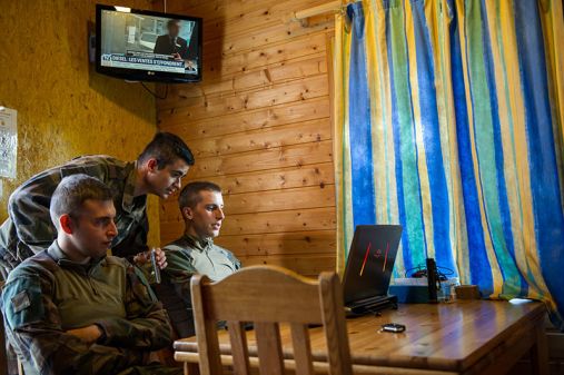 Dans un chalet du camping du Val Joly, le chef de section vient jeter un œil curieux sur l'un de ses soldats occupé à jouer à un jeu vidéo sur son ordinateur durant un temps libre.
